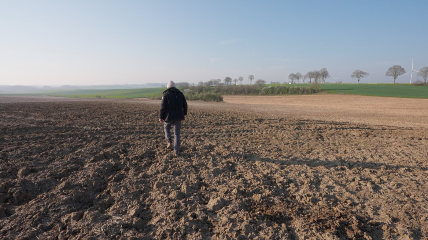Image du film · un agriculteur marche dans son champ, terre ouverte à perte de vue