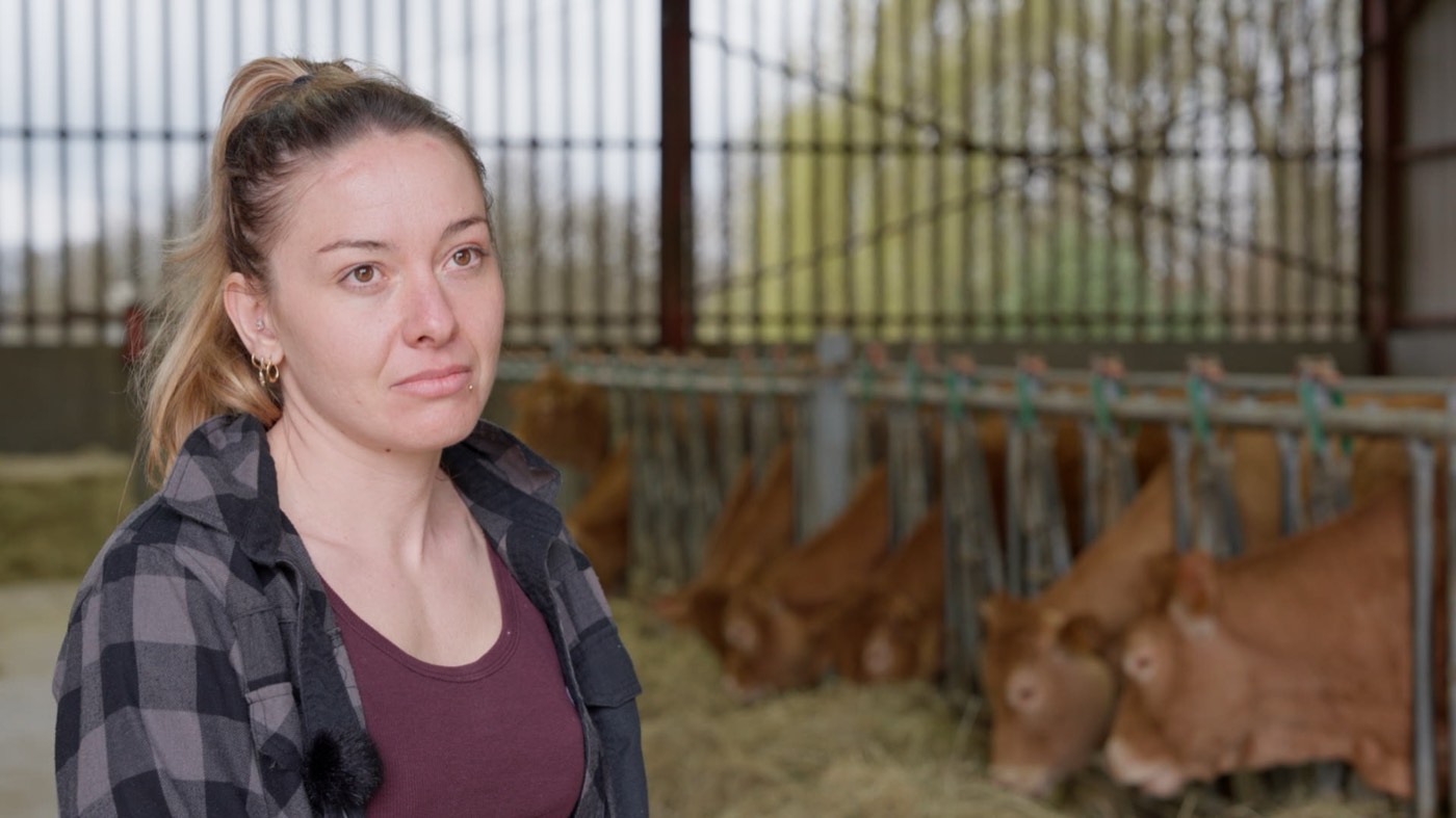 Image du film · une éleveuse dans sa stabulation, ses bêtes derrière elle